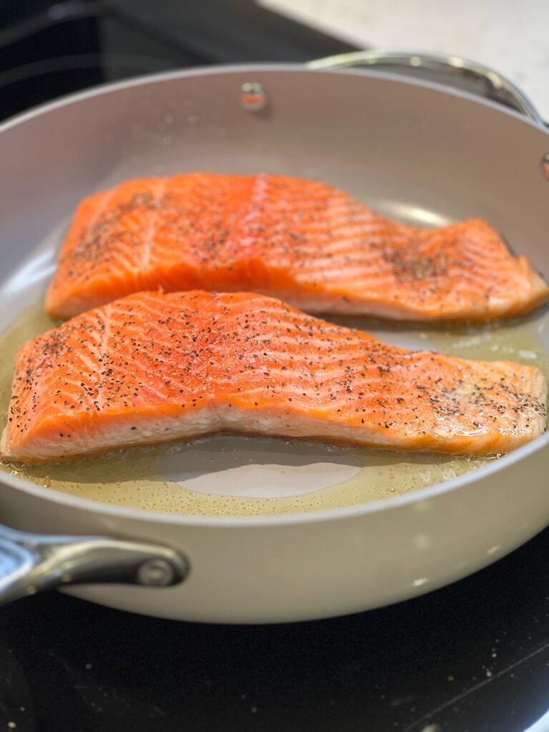 Two filets of seasoned salmon searing skin-side down in a non-stick pan with a little olive oil for Crispy Skin Salmon