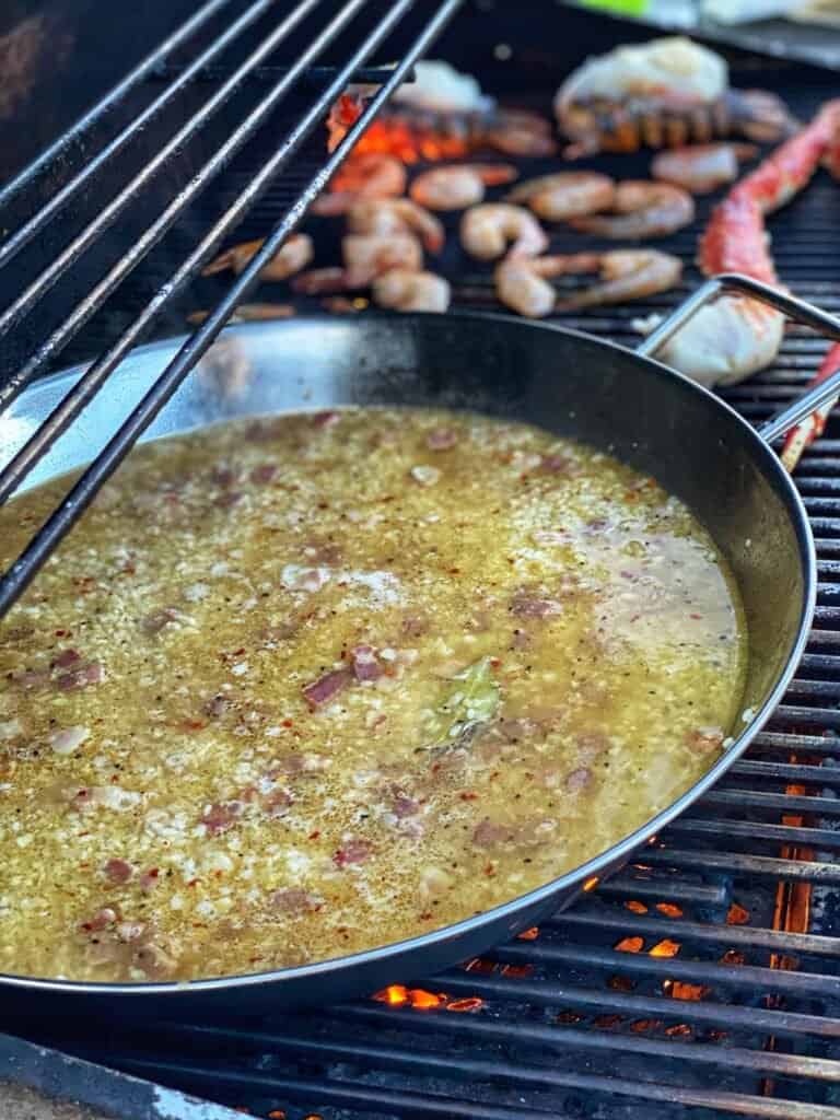 the start of easy seafood paella rice simmering in chicken stock in a paella pan on the grill