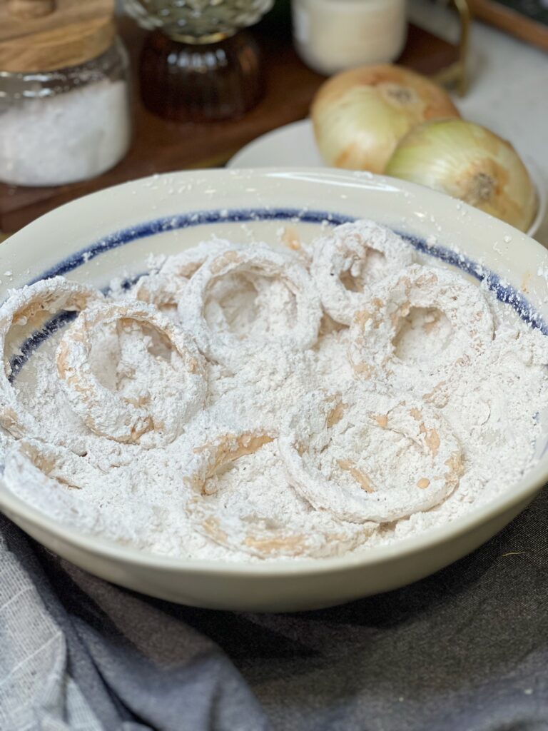 Raw, sliced Vidalia onions coated with flour in a bowl.