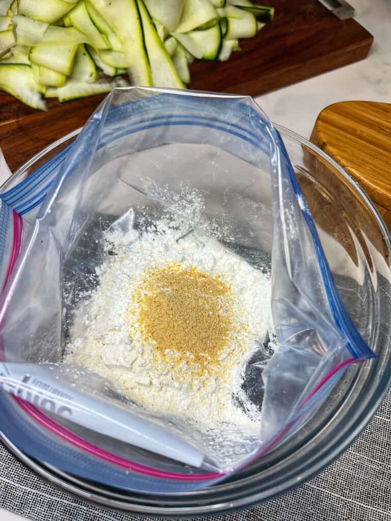 A freezer bag filled with flour and garlic powder sitting in a glass bowl.