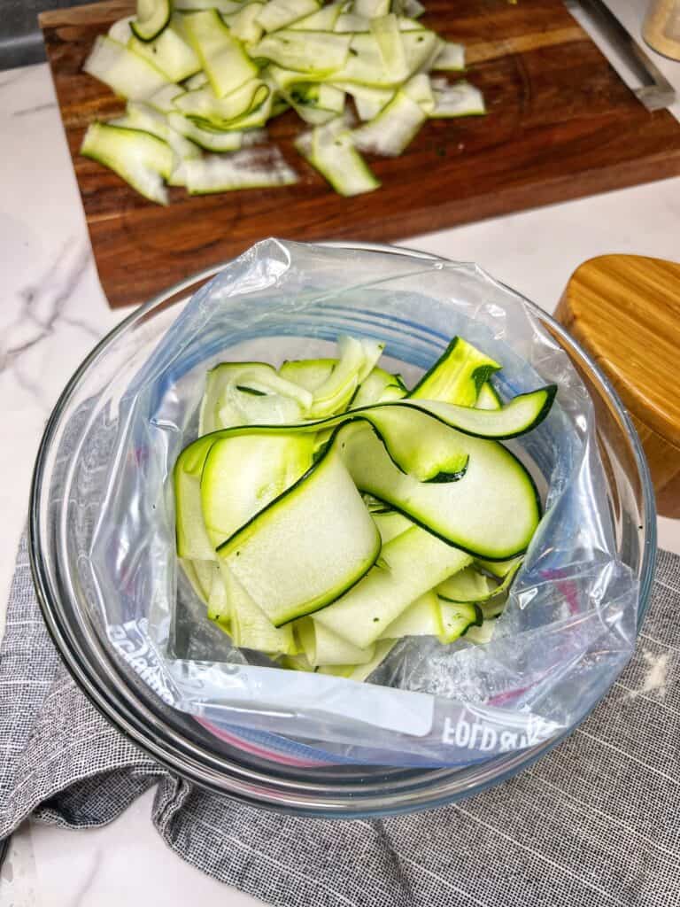 Thinly sliced zucchini in a freezer bag that is filled with flour.