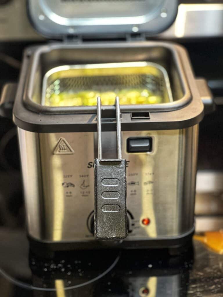 A stainless steel deep fryer that is frying zucchini ribbons.