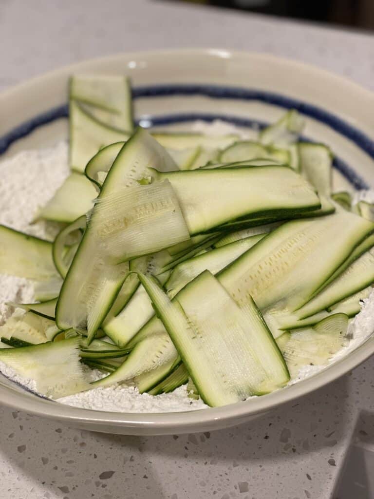 a bowl of zucchini ribbons in flour