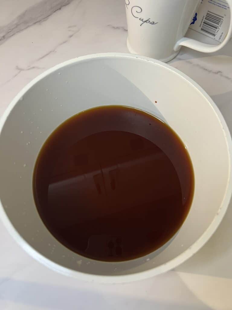 Chicken stock and soy sauce mixed together in a white sauce pot.