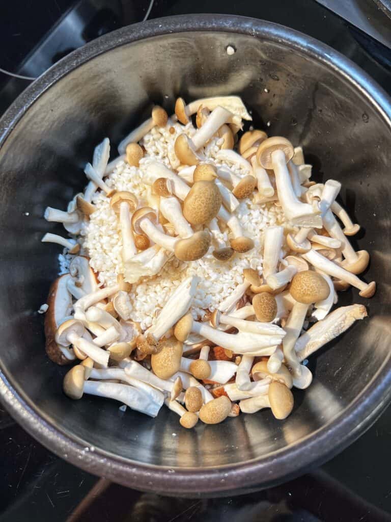 Soaked short-grain rice and brown beech mushrooms in a brown clay pot for Kamameshi with Mushrooms