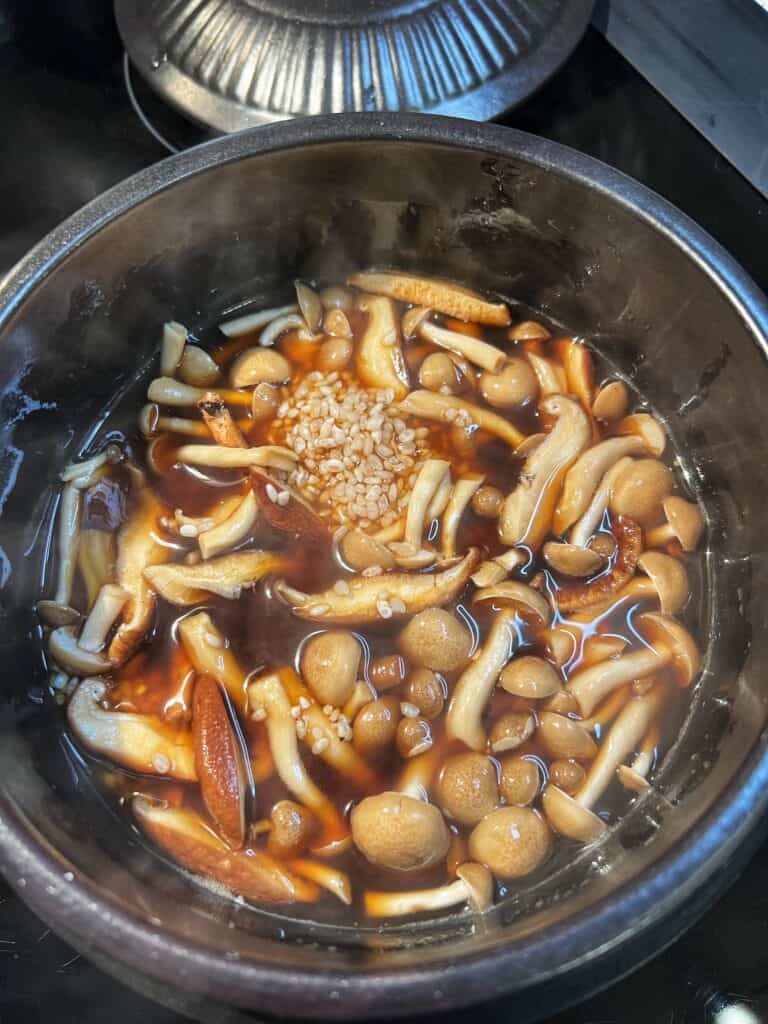 Rice, mushrooms, stock and soy sauce getting ready to simmer in a clay pot.