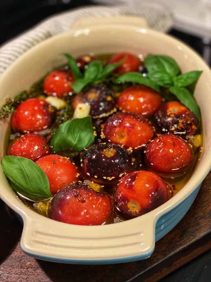 a blue oven safe dish filled with fresh tomatoes, basil, garlic and olive oil for confit tomatoes and garlic