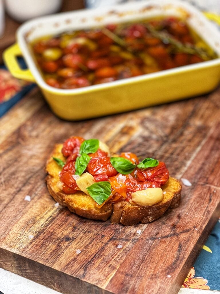 Tomato and garlic confit on toast garnished with fresh basil leaves. The tomatoes are garlic have been slow roasted.