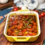 A small yellow, rectangular casserole dish holding tomato and garlic confit. They have been slow roasted in olive oil with fresh rosemary.