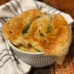a medium-sized white ramekin filled with broccoli chicken pot pie topped with a flaky puff pastry and garnished with fresh chopped parsley