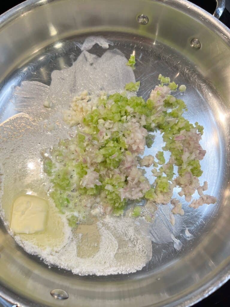 Minced celery, shallots and garlic sautéing in butter in a stainless steel pan.