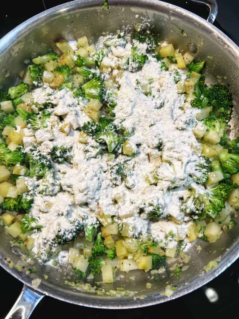 Flour sprinkled over diced potatoes and broccoli in a pan.
