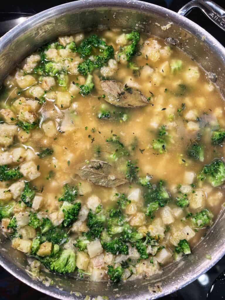 Chicken stock and bay leaves added to a pan with broccoli and diced potatoes.