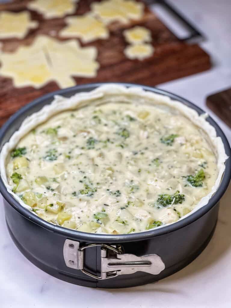 A springform pan lined with pastry dough and filled with a broccoli chicken cream mixture.