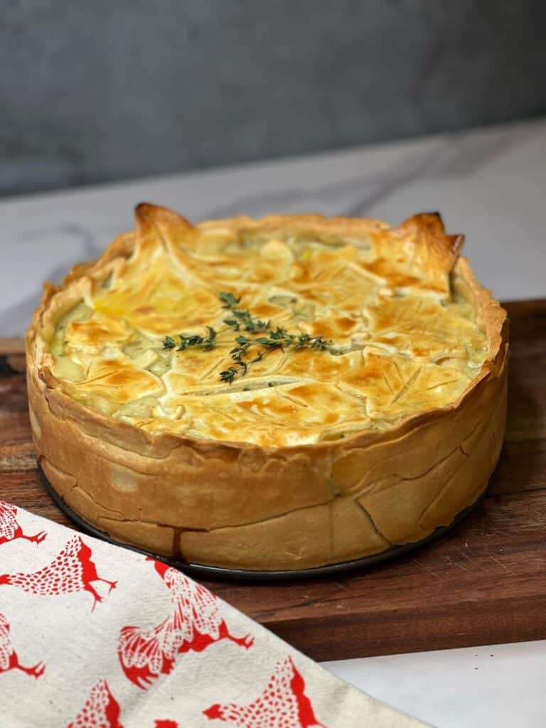 A large broccoli chicken pot pie sitting on top of a wooden cutting board and garnished with fresh thyme.