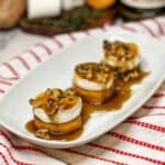 A white plate of three fondant sweet potatoes topped with maple butter walnuts.