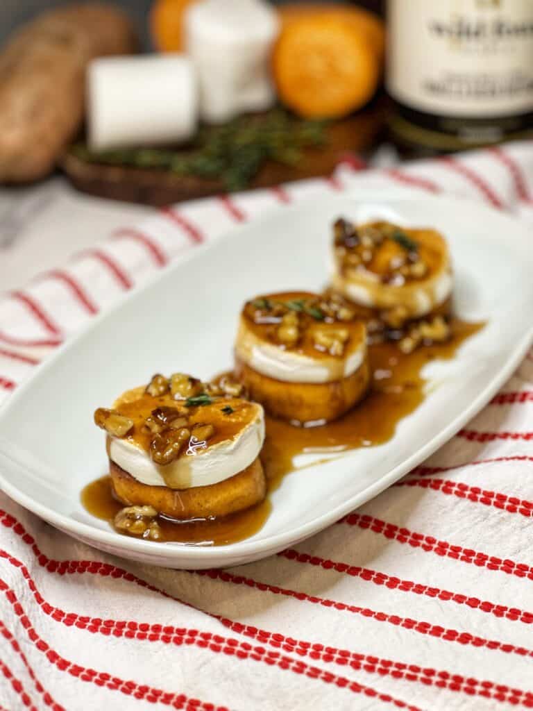 A white plate of three fondant sweet potatoes topped with maple butter walnuts.