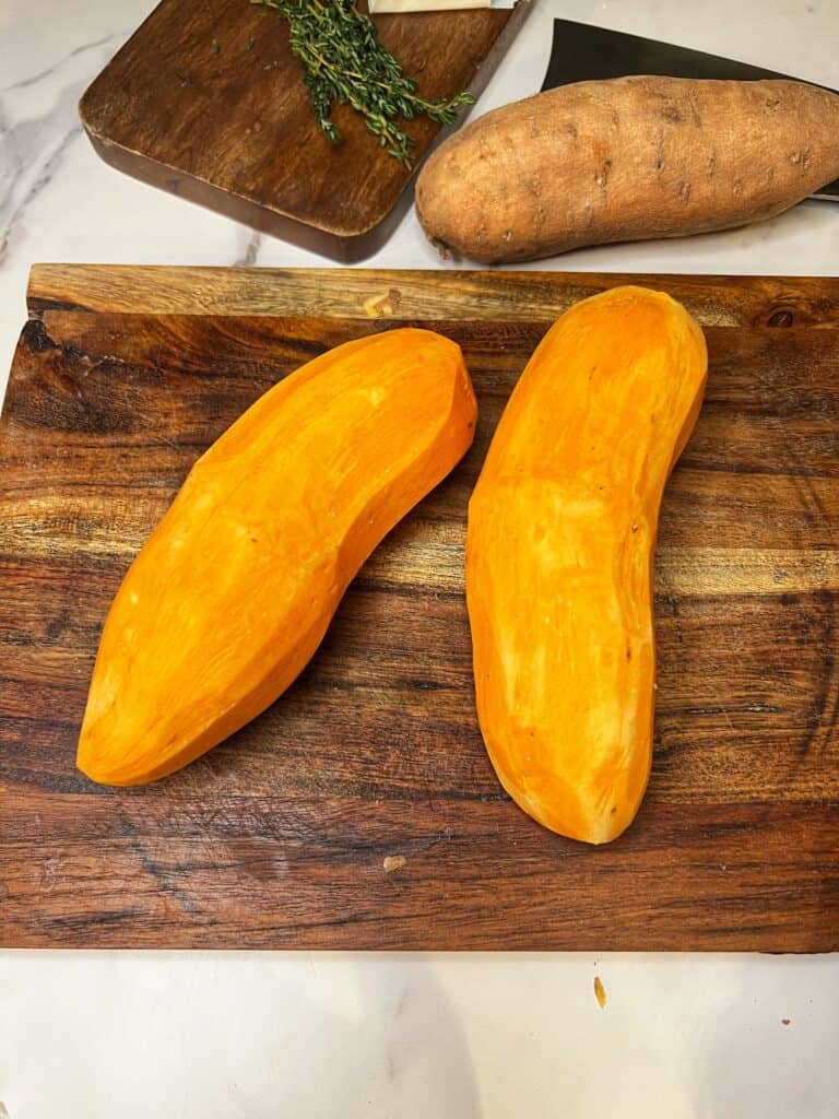 Two peeled sweet potatoes sitting on a wooden board.