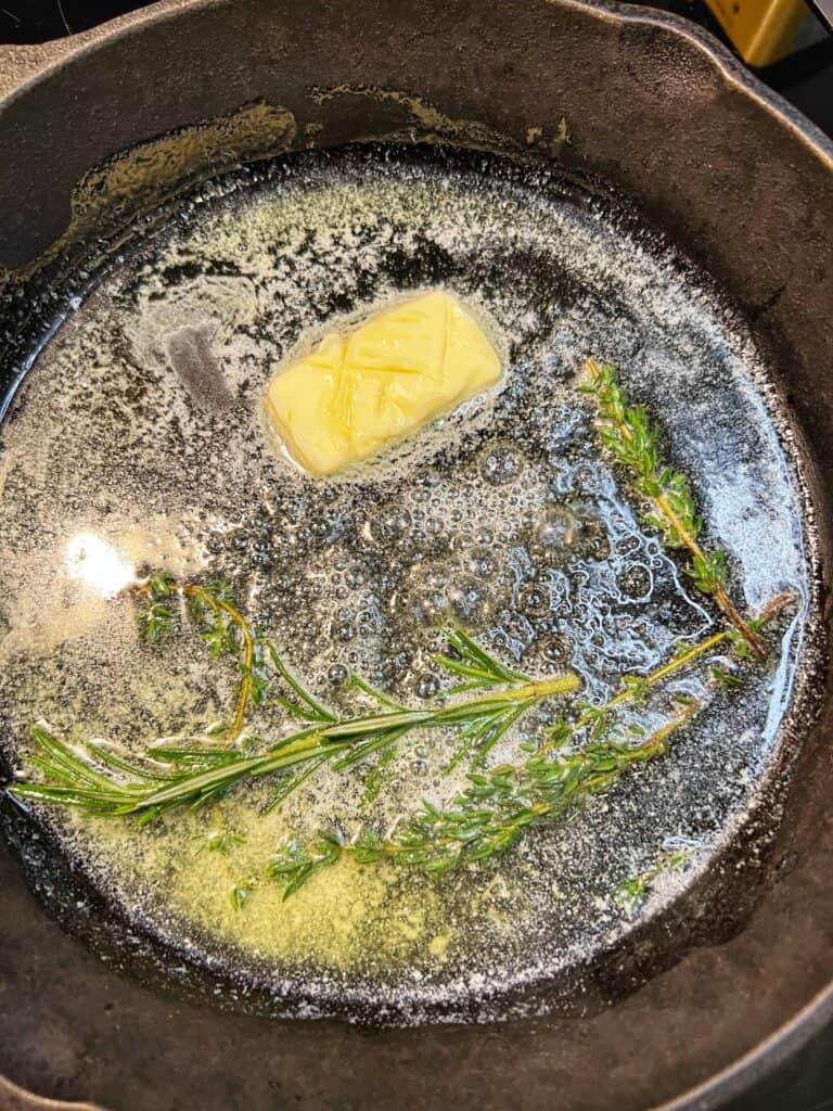 Butter and olive oil heating in a cast iron pan with fresh rosemary and fresh thyme. 