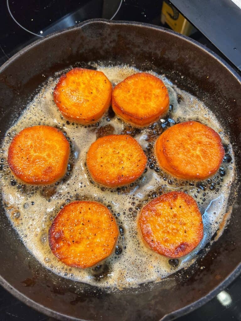 Browning round pieces of sweet potato in a cast iron pan.