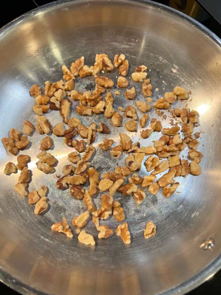 Walnut pieces toasting in a stainless steel pan.
