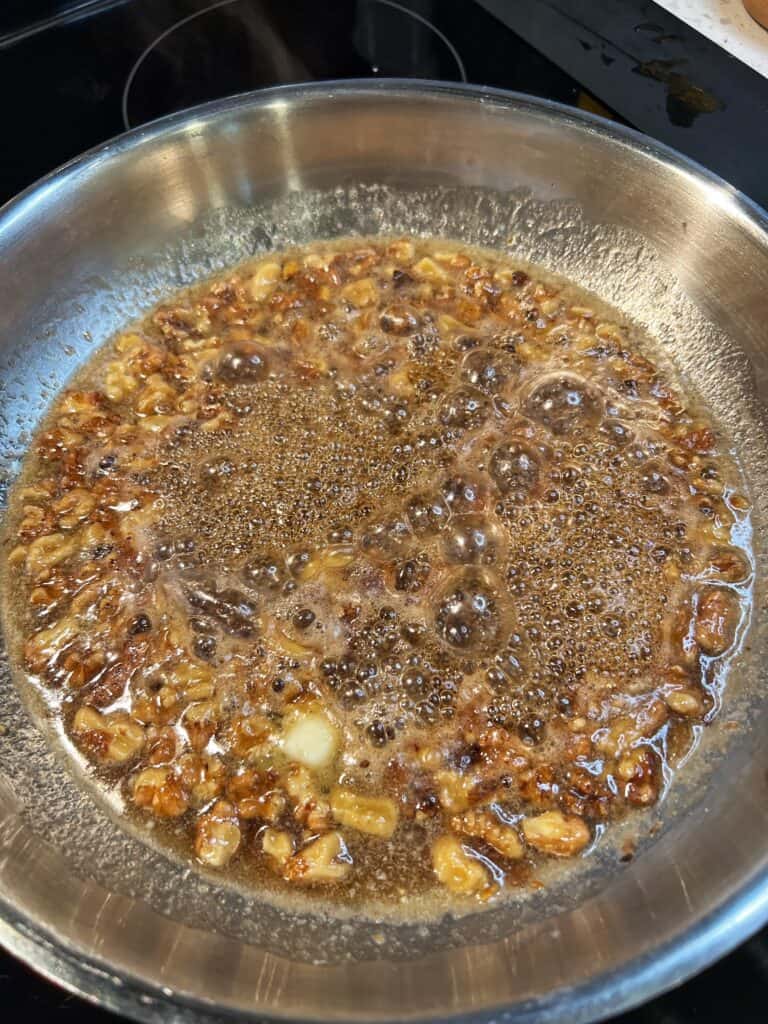 Simmering maple butter walnuts in a stainless steel pan.