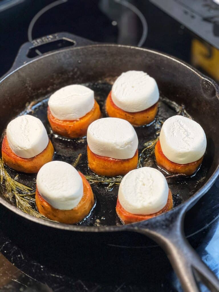 Fondant sweet potatoes in a cast iron pan topped each with a piece of marshmallow.