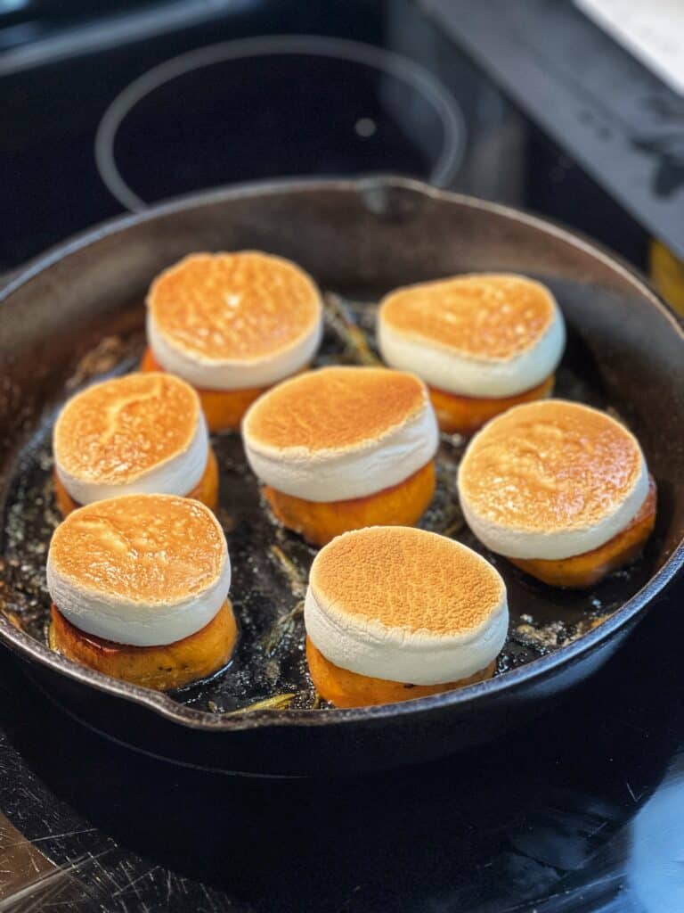 Fondant sweet potatoes in a cast iron pan, each topped with a piece of toasted marshmallow.