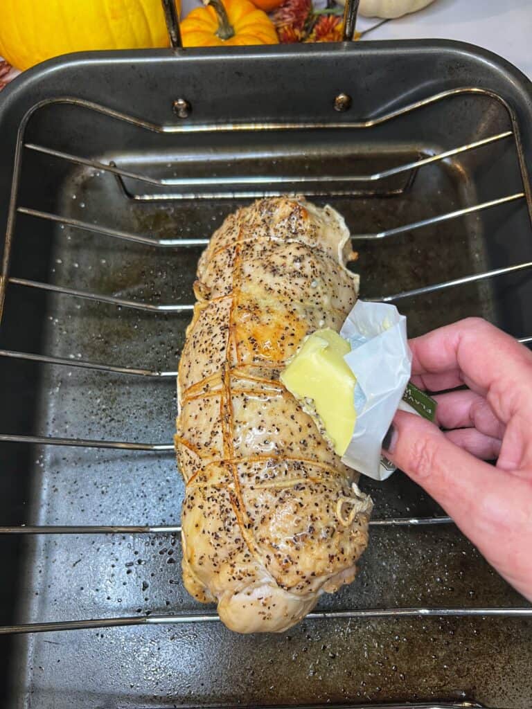 Me rubbing a partially cooked turkey roulade with butter as it's sitting on a roasting rack in a roasting pan.