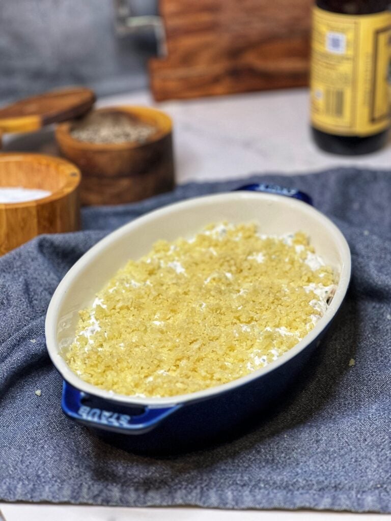 A small blue casserole dish filled with creamy hot clam dip that is topped with a butter panko topping. The dip is not yet baked.