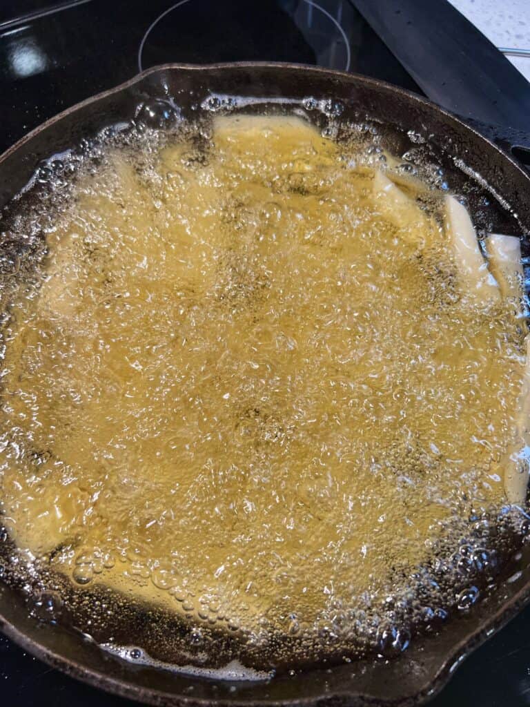 Chips, or thick-cut fries frying for the first fry in a cast iron skillet.