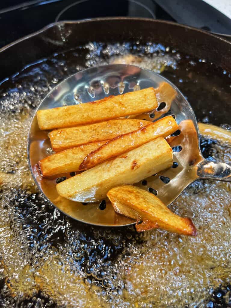 A slotted spoonful of golden brown and crispy chips, or thick-cut potatoes.