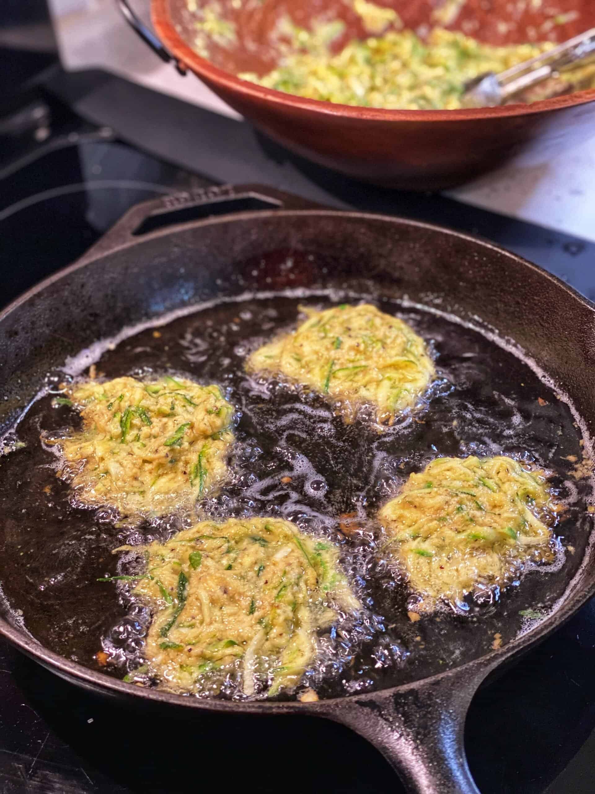 four Crispy Italian Zucchini Fritters frying in a cast iron pan
