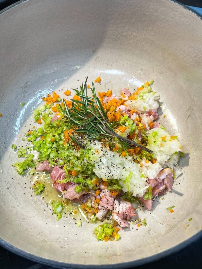 Diced bacon, minced celery, onion and carrots and a sprig of rosemary in a soup pot.