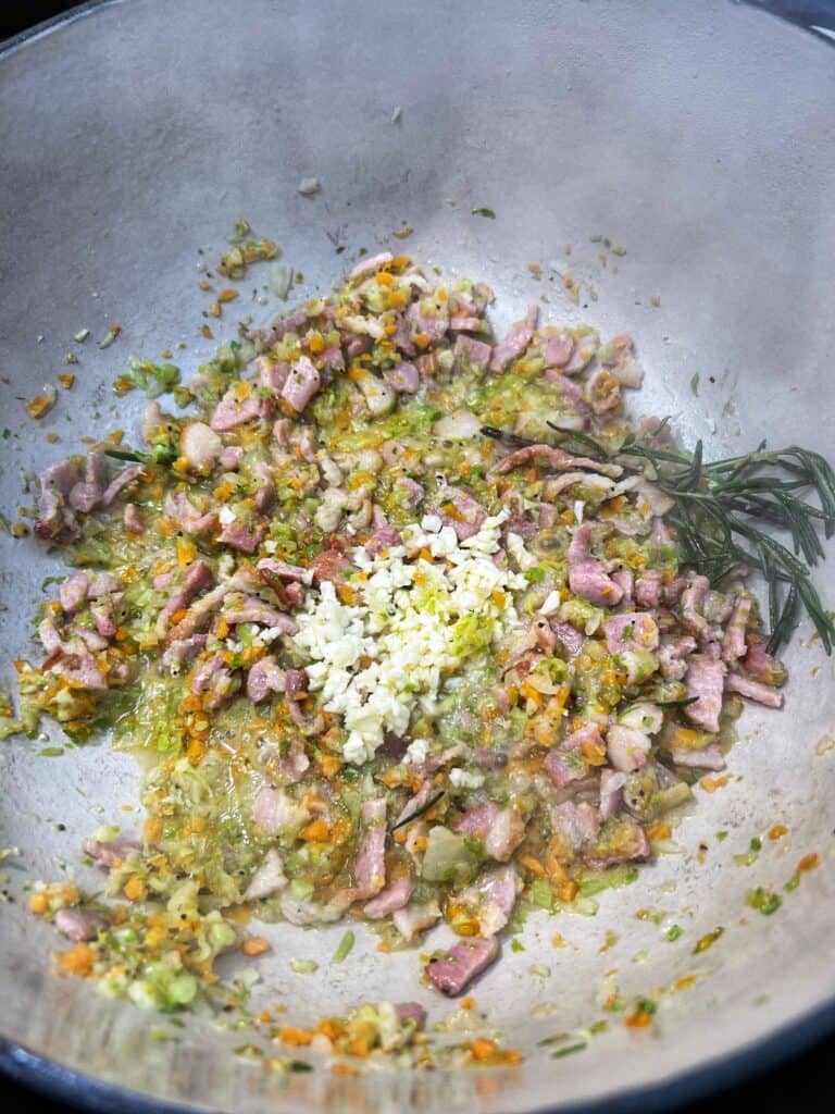 Softened vegetables and bacon with minced garlic in a pot for Fagioli.