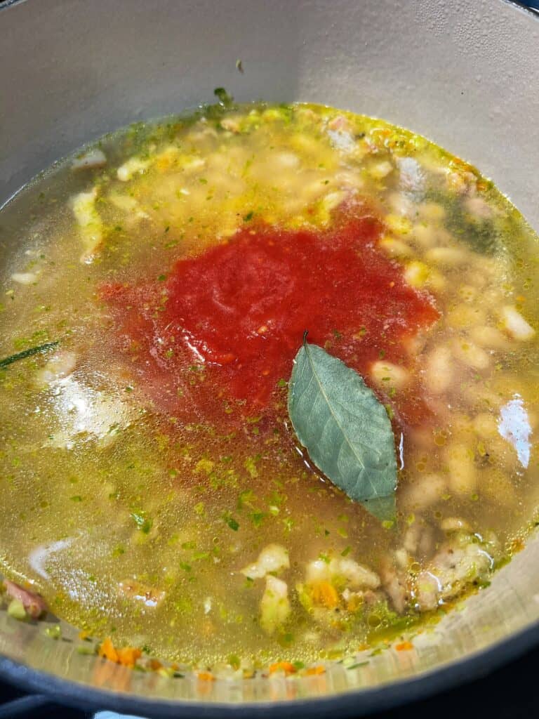 Cannelini beans, crushed tomatoes, chicken stock and a bay leaf added to softened vegetables in a pot to make pasta fagioli