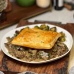 A white shallow bowl of beef tips in cream sauce with mushrooms. The dish is topped with a square of baked puff pastry.