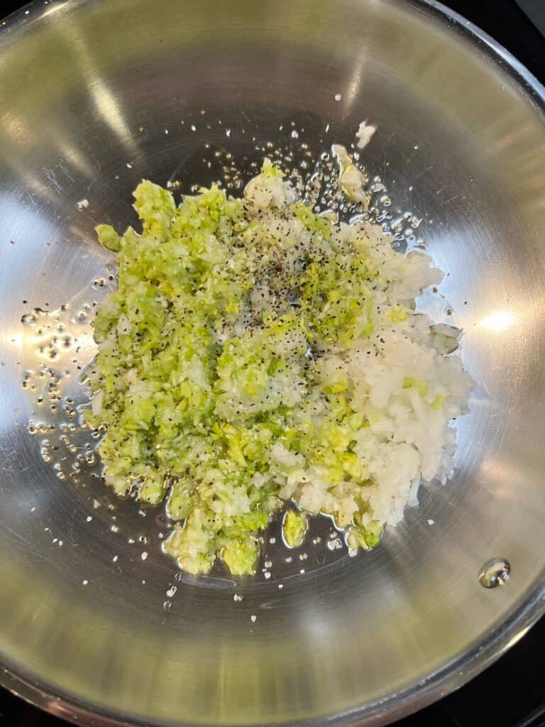 Minced celery and minced onions sautéing in a pan with olive oil.