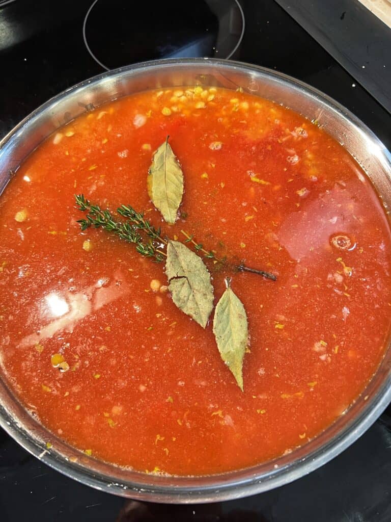 Tomatoes, bay leaves and fresh herbs added to a pan of lentils.