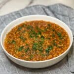 A white bowl filled with tomato braised lentils that are garnished with fresh parsley.