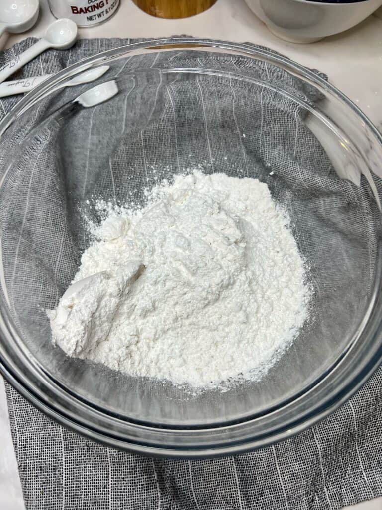 A glass bowl of flour, baking powder and salt for super fluffy blueberry pancakes.