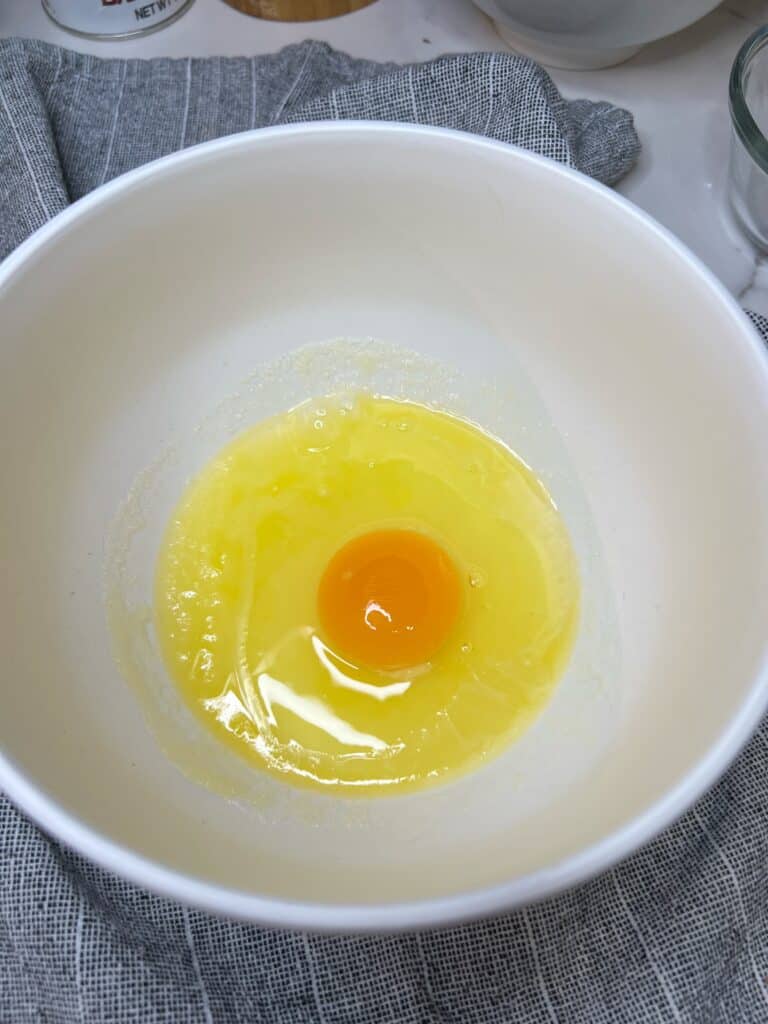 One egg in a white bowl of melted butter and sugar.