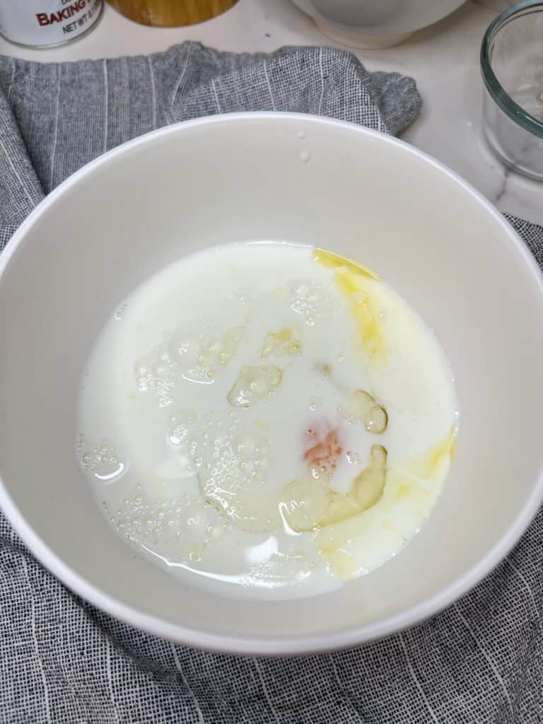 Milk in a white bowl of a butter, sugar and egg mixture.