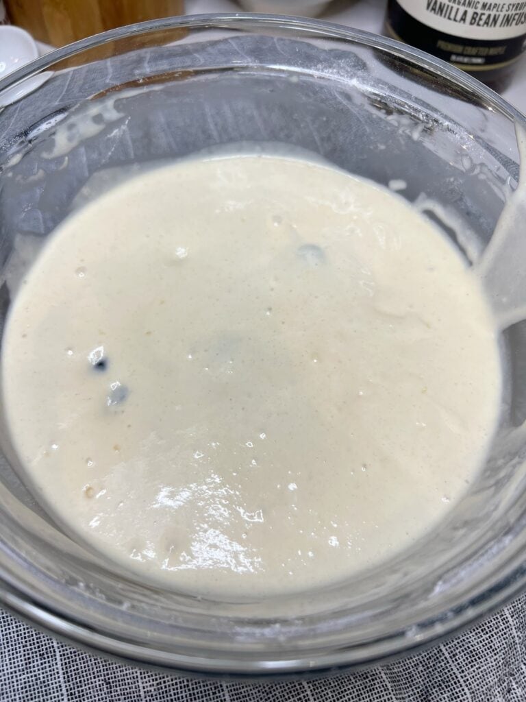 Rested blueberry pancake batter in a glass bowl.