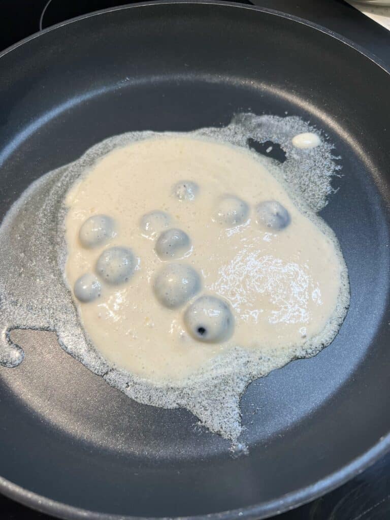 One blueberry pancake starting to cook in butter in a non-stick pan.