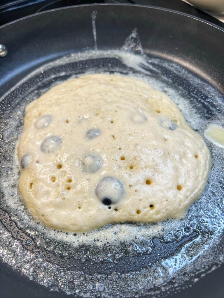 Significant bubbles forming on the top of a blueberry pancake that is ready to flip.
