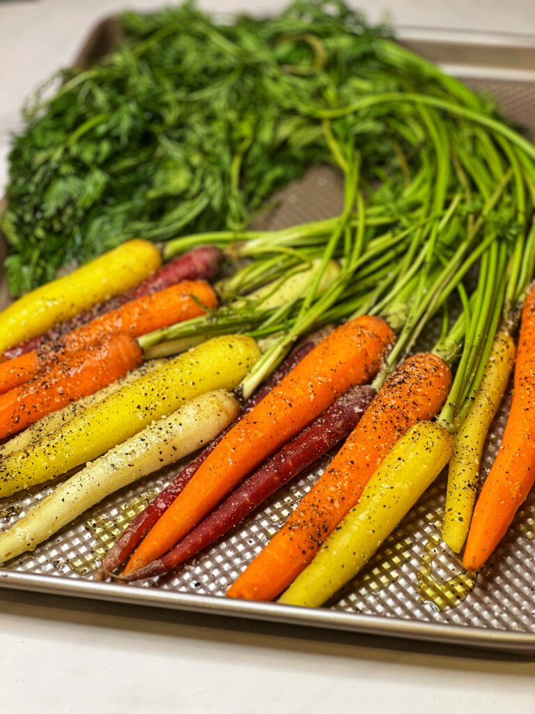 A bunch of colored carrots seasoned with salt and pepper laying on a gold baking sheet.