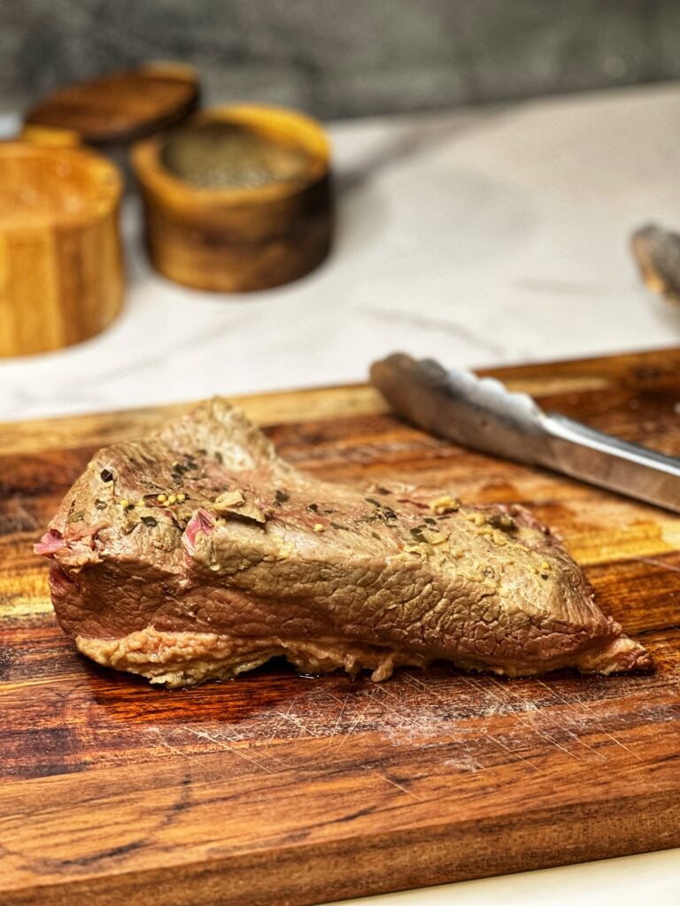 A slow-cooked piece of corned beef laying on a wooden cutting board.