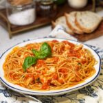 A large bowl of spicy lobster pasta pomodoro. Chunks of poached lobster in a tomato sauce is tossed with spaghetti and garnished with fresh basil.
