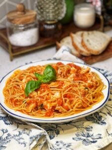 A large bowl of spicy lobster pasta pomodoro. Chunks of poached lobster in a tomato sauce is tossed with spaghetti and garnished with fresh basil.
